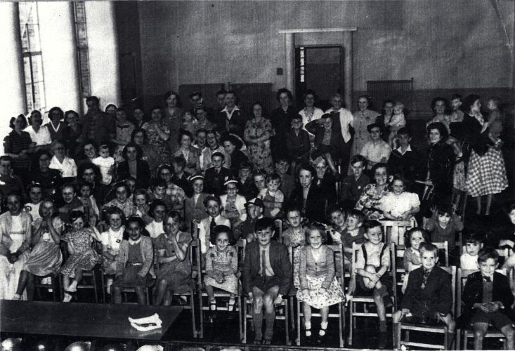 This is a picture of an event held at the school during the 1950s. At the back of the hall, the door to the foyer is open; the flower arrangement on the polished table being just visible. The closed doors on the left led into the dining room. | Taken from a photograph in Robin Safe's possession.